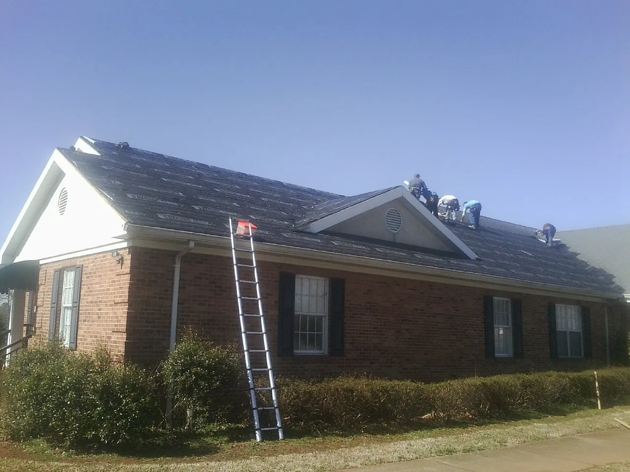 Crew tearing shingles off a brick ranch roof with a ladder set — Emergency Roof Repair work by our crew in Pembroke